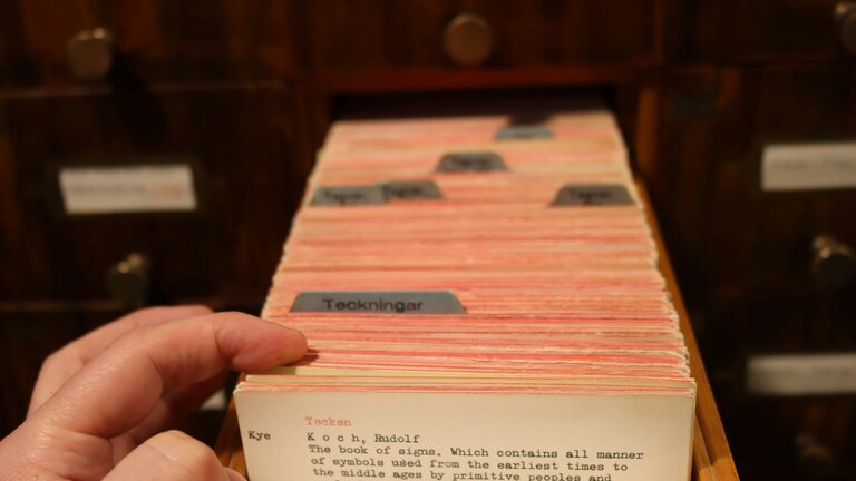A hand pulling a card from a library card catalog